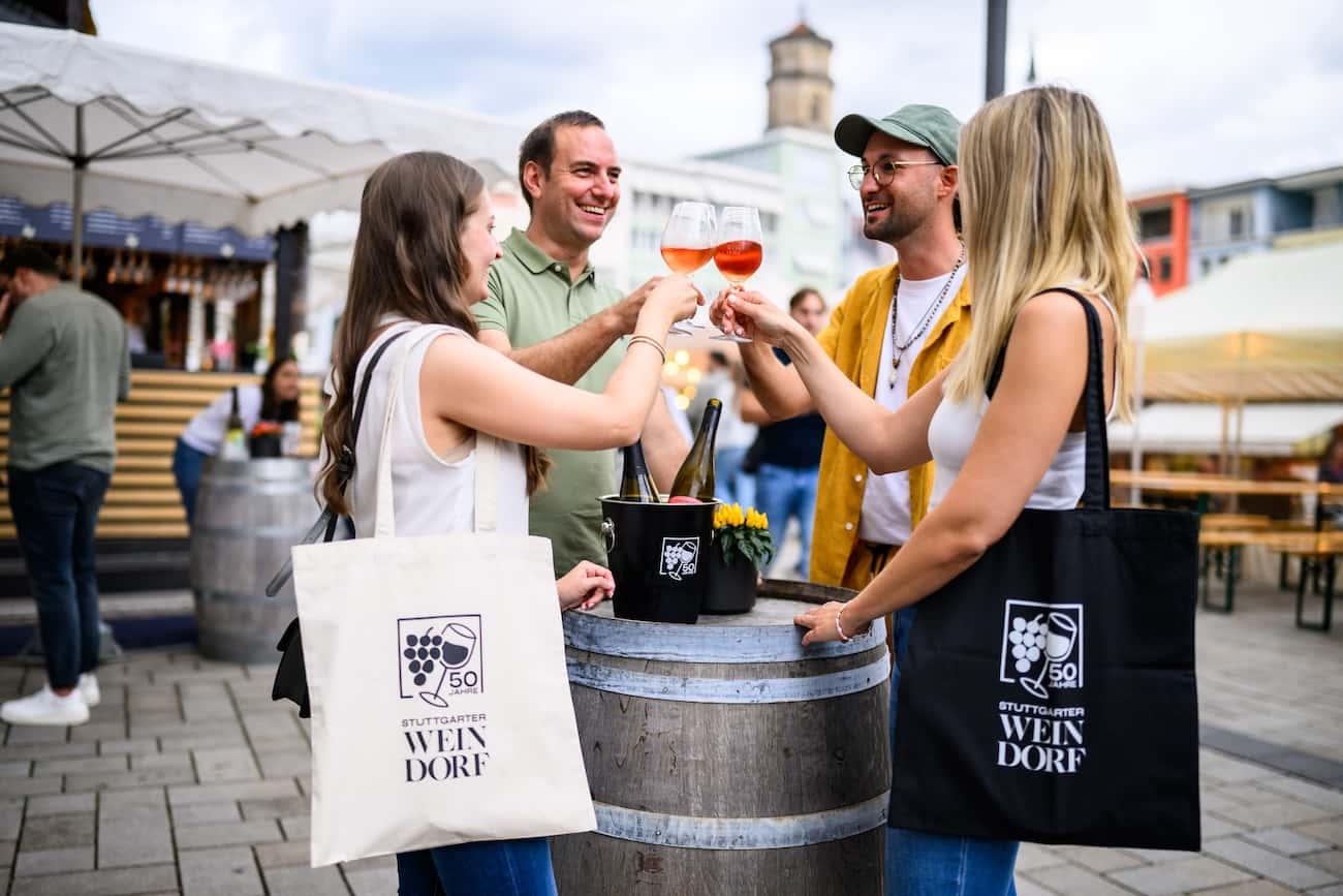 Vier Personen stehen anstoßend mit Gläsern Wein um einen Fasstisch auf dem Stuttgarter Weindorf.